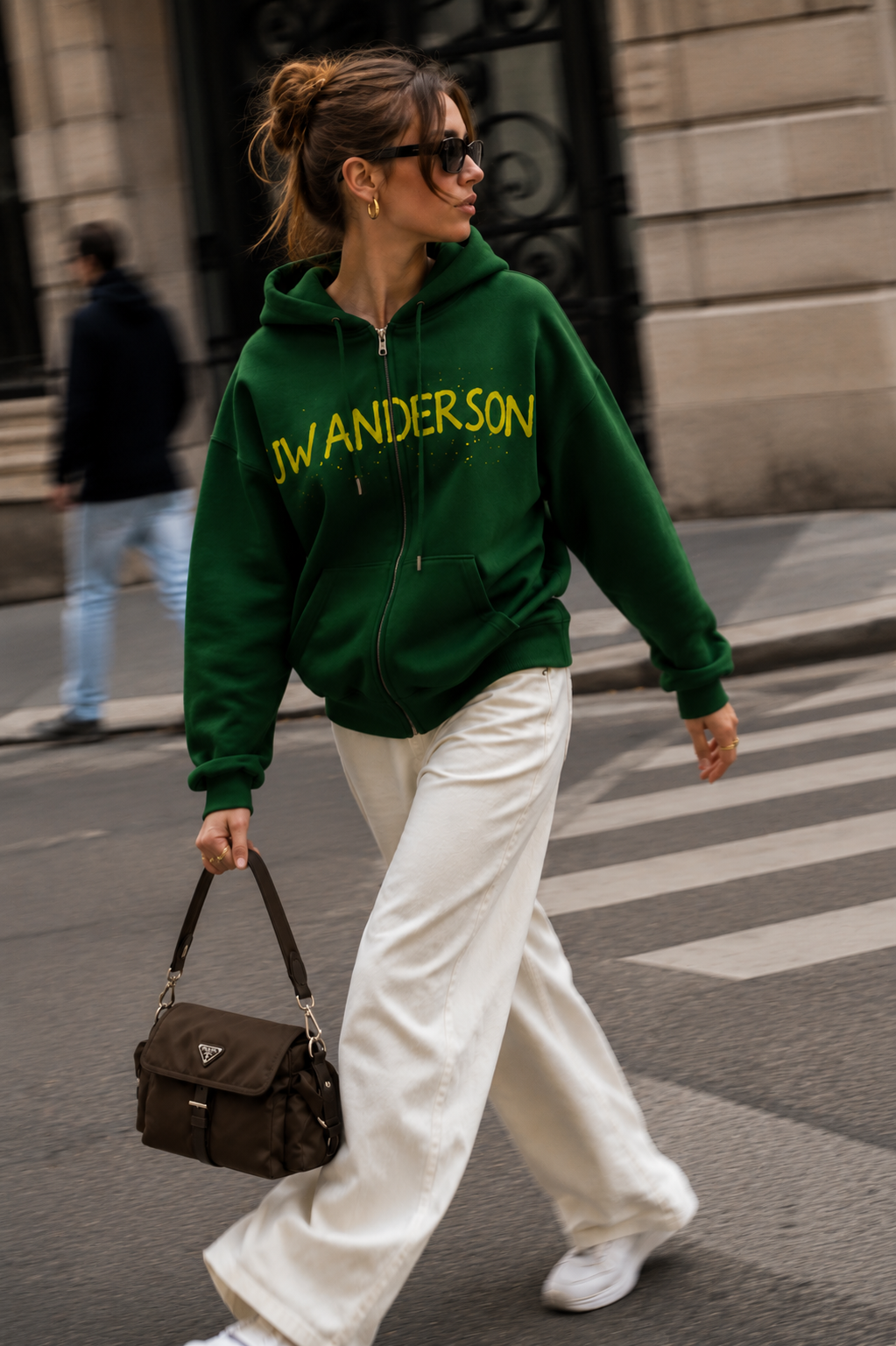 Woman in a green zip hoodie and ecru wide-leg trousers crossing a Paris street