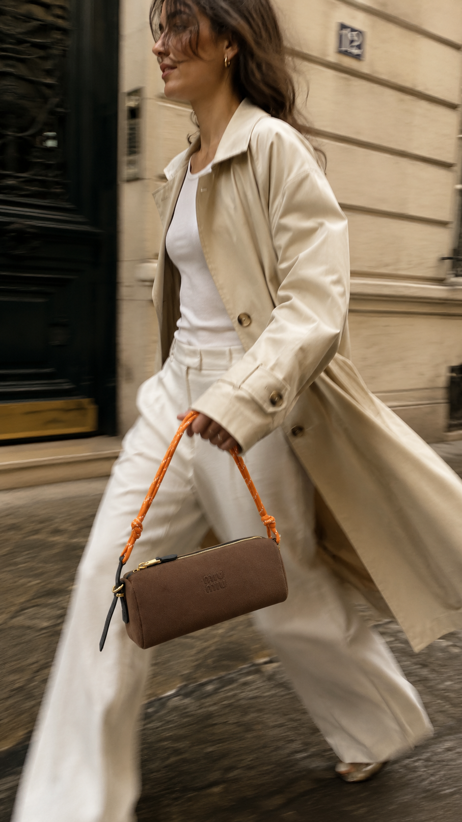 Woman walking a Paris street in a cream trench coat with a brown canvas shoulder bag