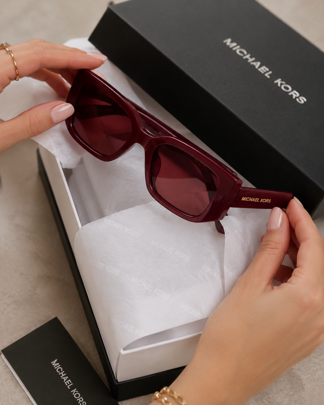 Hands unboxing burgundy rectangular sunglasses from a black designer gift box